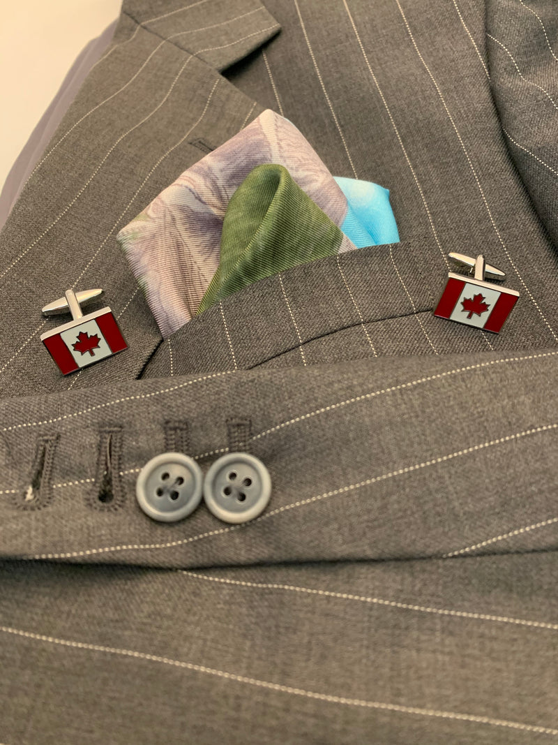 Pocket square with drawing of three mountains blue sky and green grass folded in men's grey pinstripe blazer flanked by Canadian Rogue cufflinks