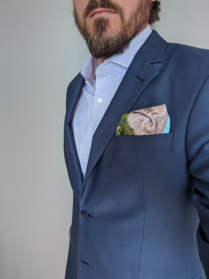 Pocket square with drawing of three mountains blue sky and green grass folded in men's blue blazer